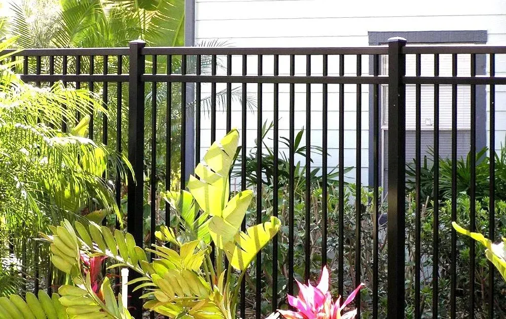 A black metal fence surrounds a lush green garden.