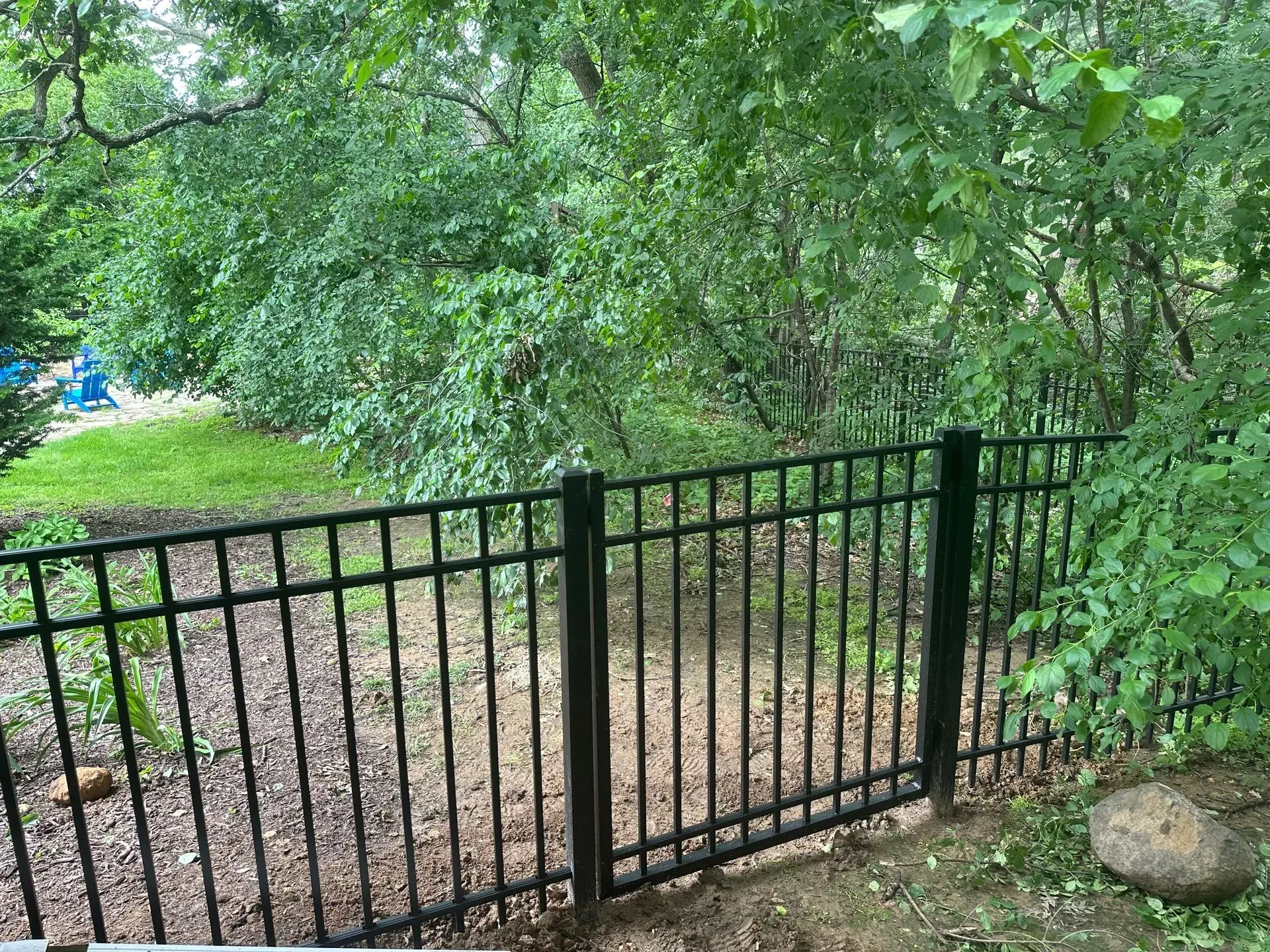 A black metal fence is surrounded by trees in a yard.