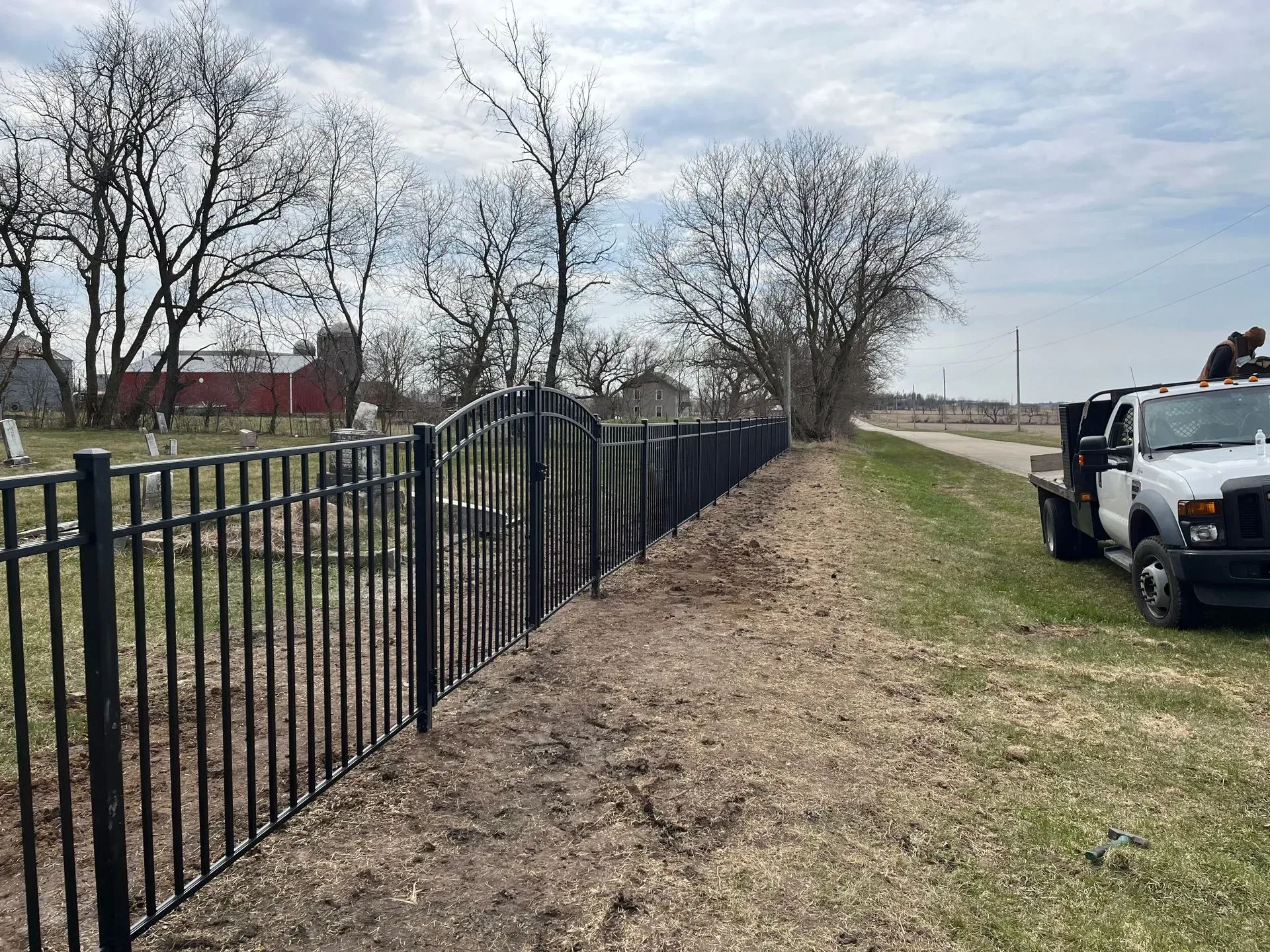A white truck is parked next to a black fence in front of a cemetery.