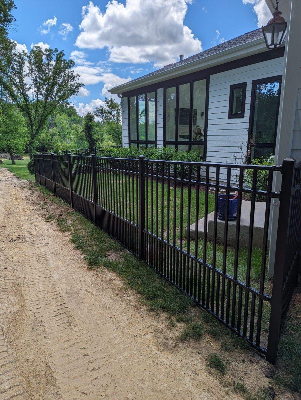 A black fence surrounds a white house on a dirt road.