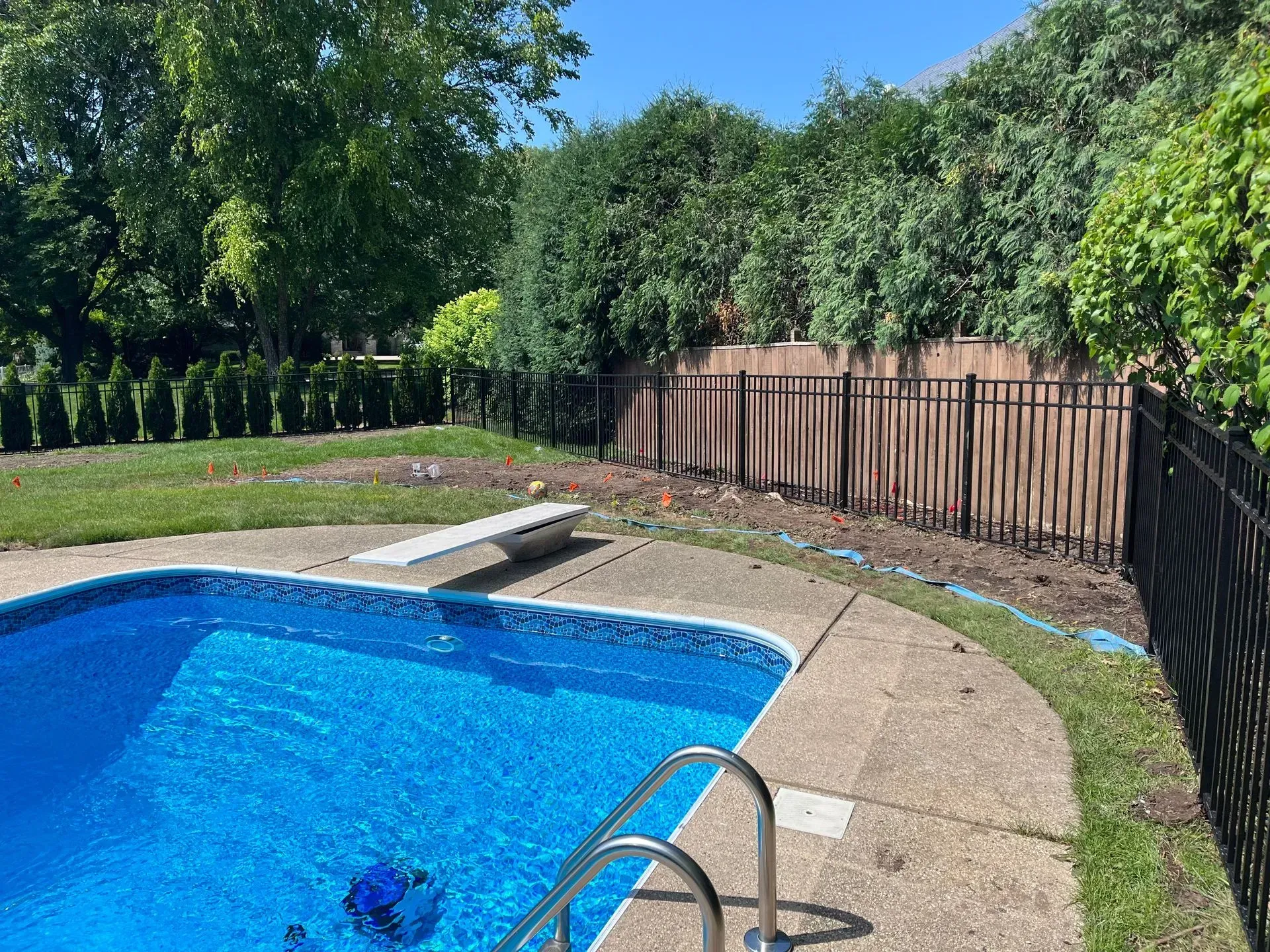There is a swimming pool in the backyard with a black fence surrounding it.