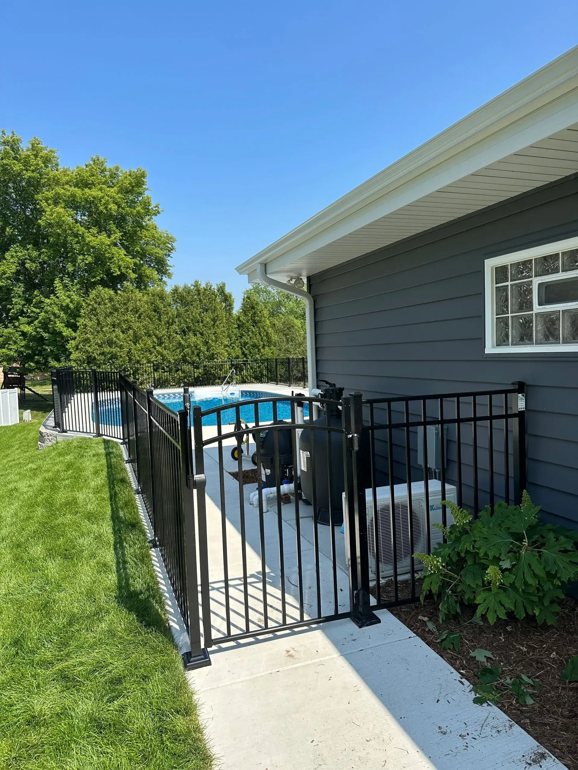 A black fence surrounds a swimming pool in front of a house.