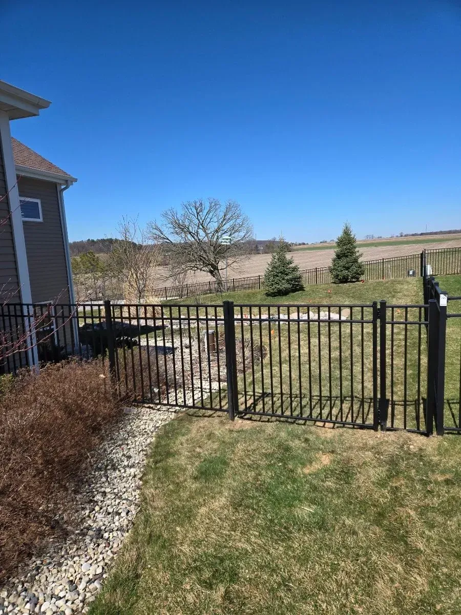 A black fence surrounds a lush green yard in front of a house.