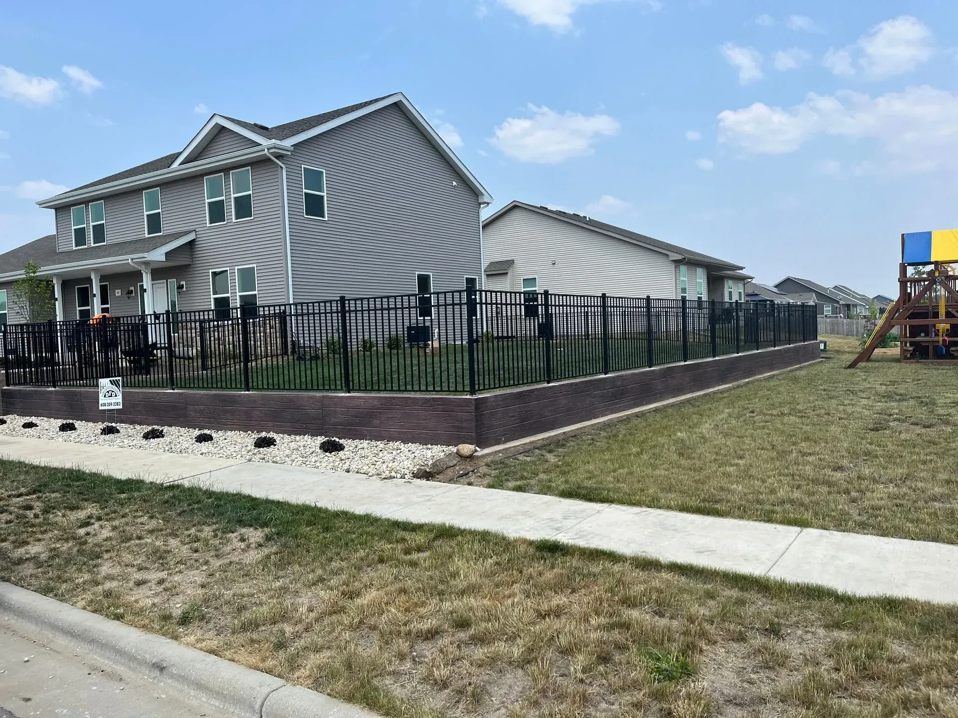 A house with a fence around it and a playground in front of it.