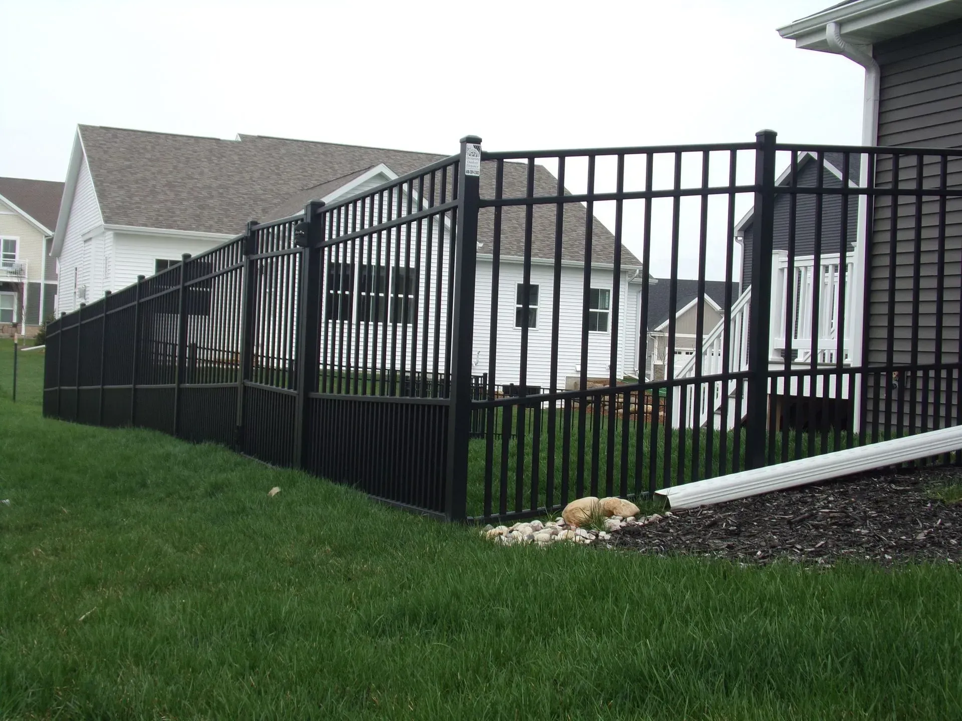 A black fence surrounds a lush green yard in front of a house