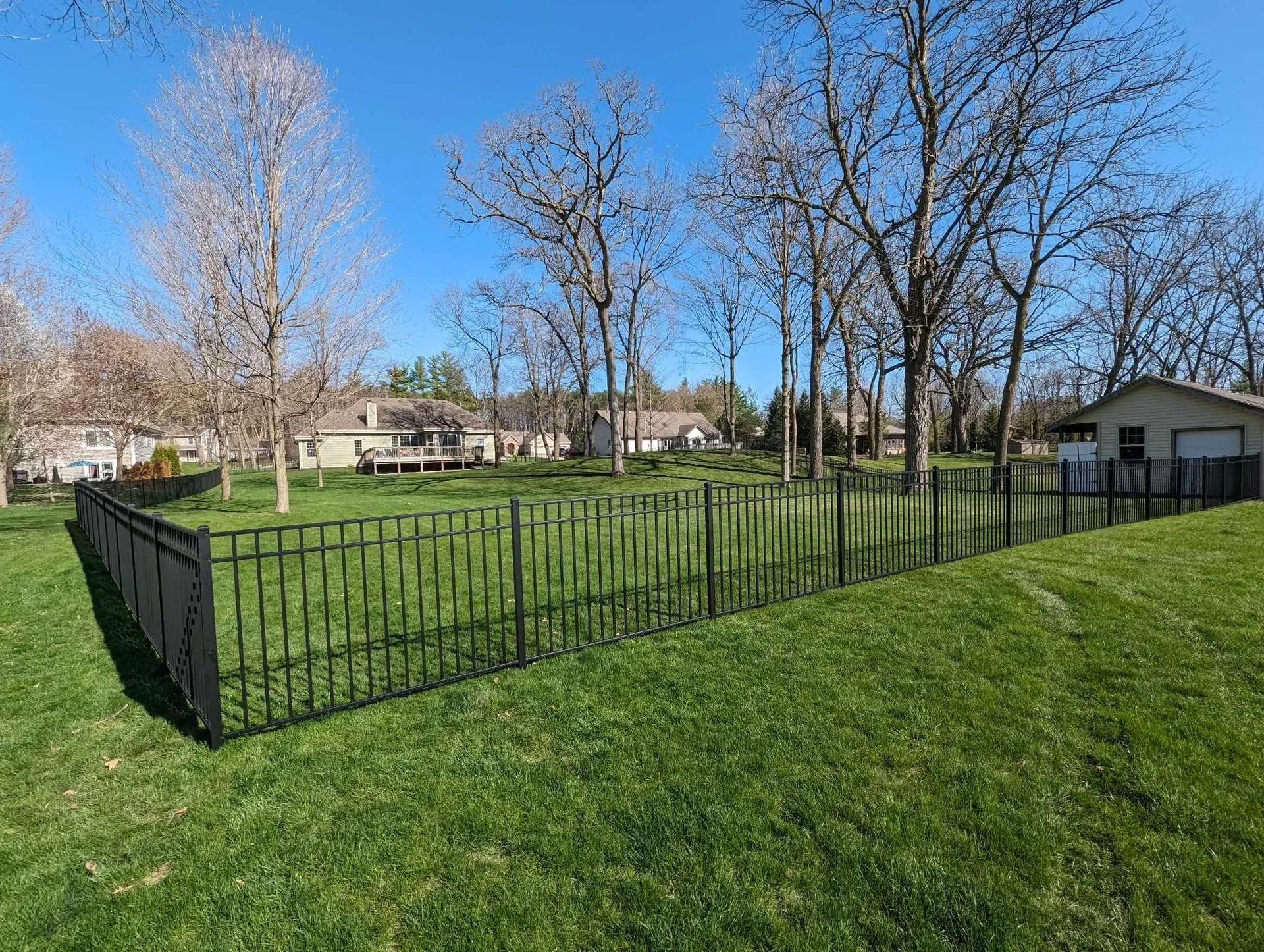 A fence surrounds a lush green field with trees in the background.