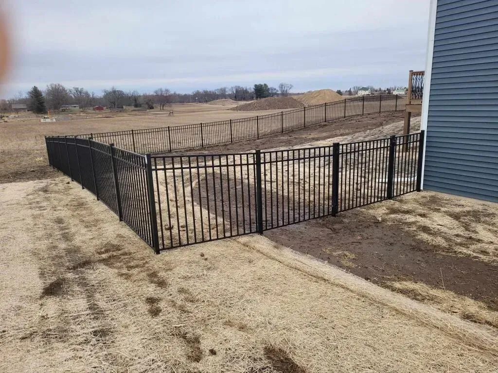 A black fence is surrounding a dirt field next to a house.