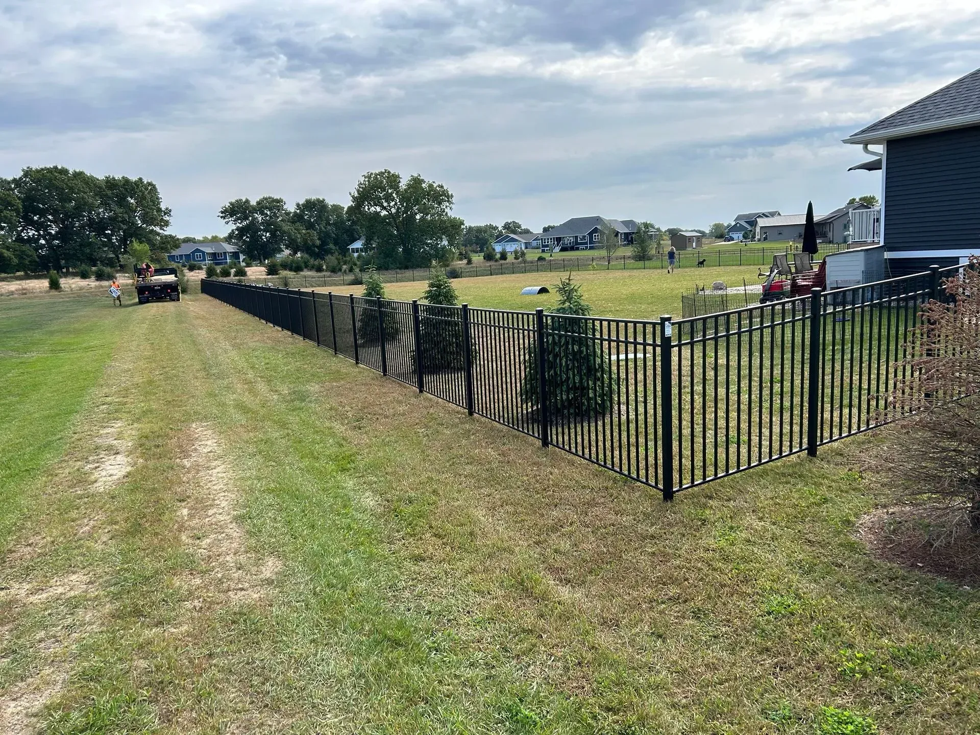 A black fence surrounds a grassy field next to a house.