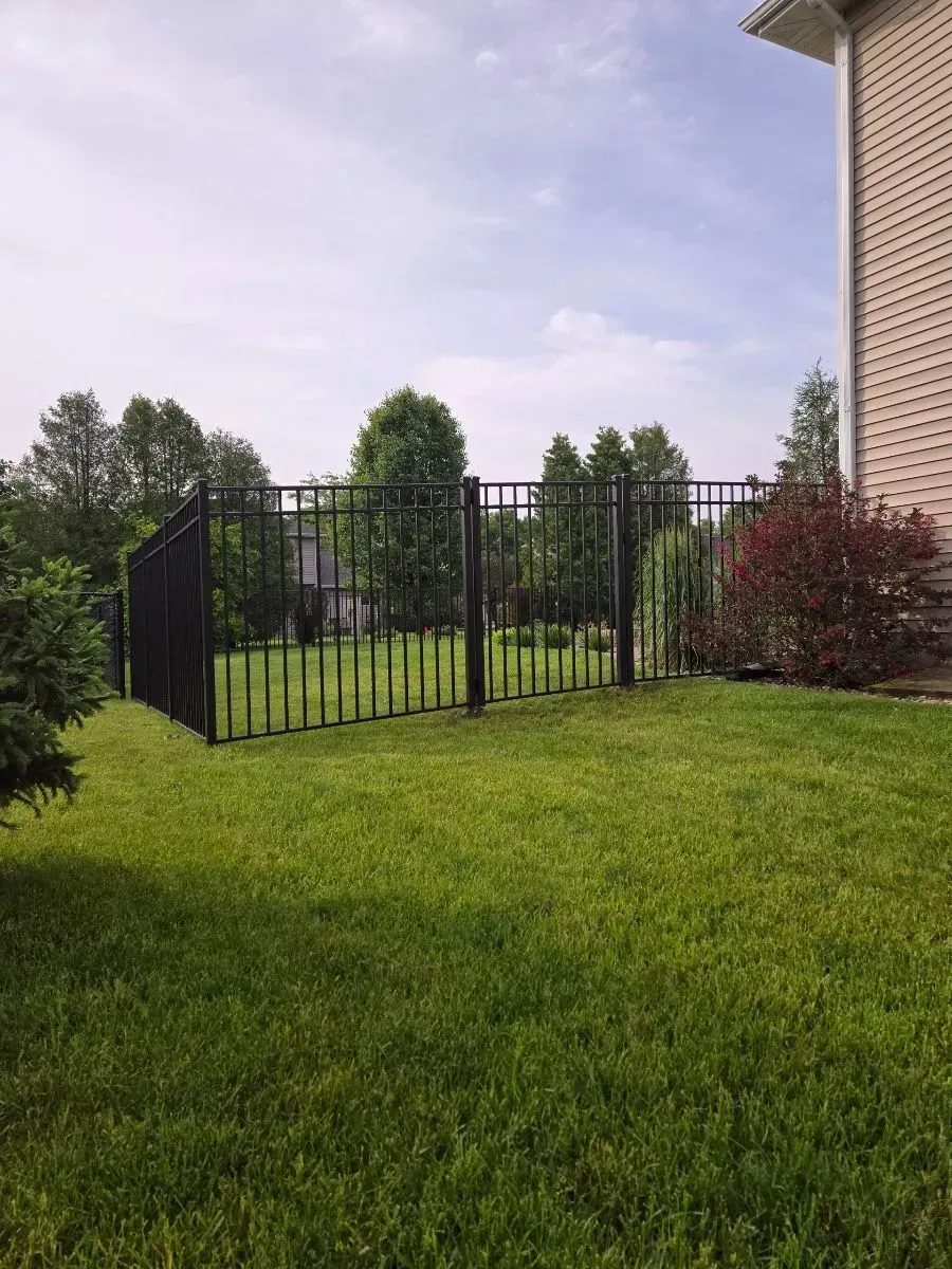 A black fence surrounds a lush green yard in front of a house.