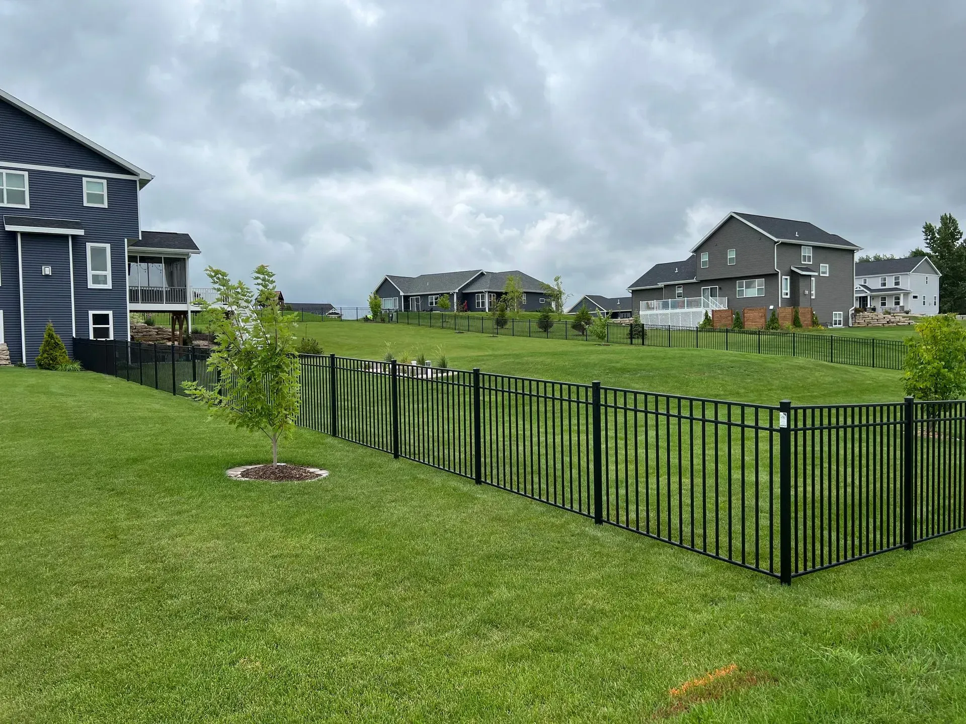 A fence surrounds a lush green field with houses in the background.