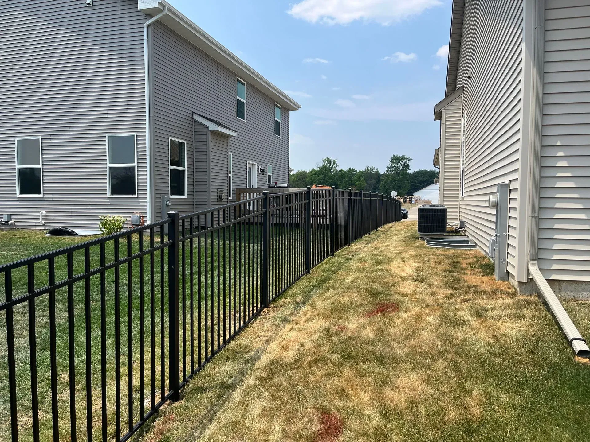 A black fence surrounds a yard between two houses.