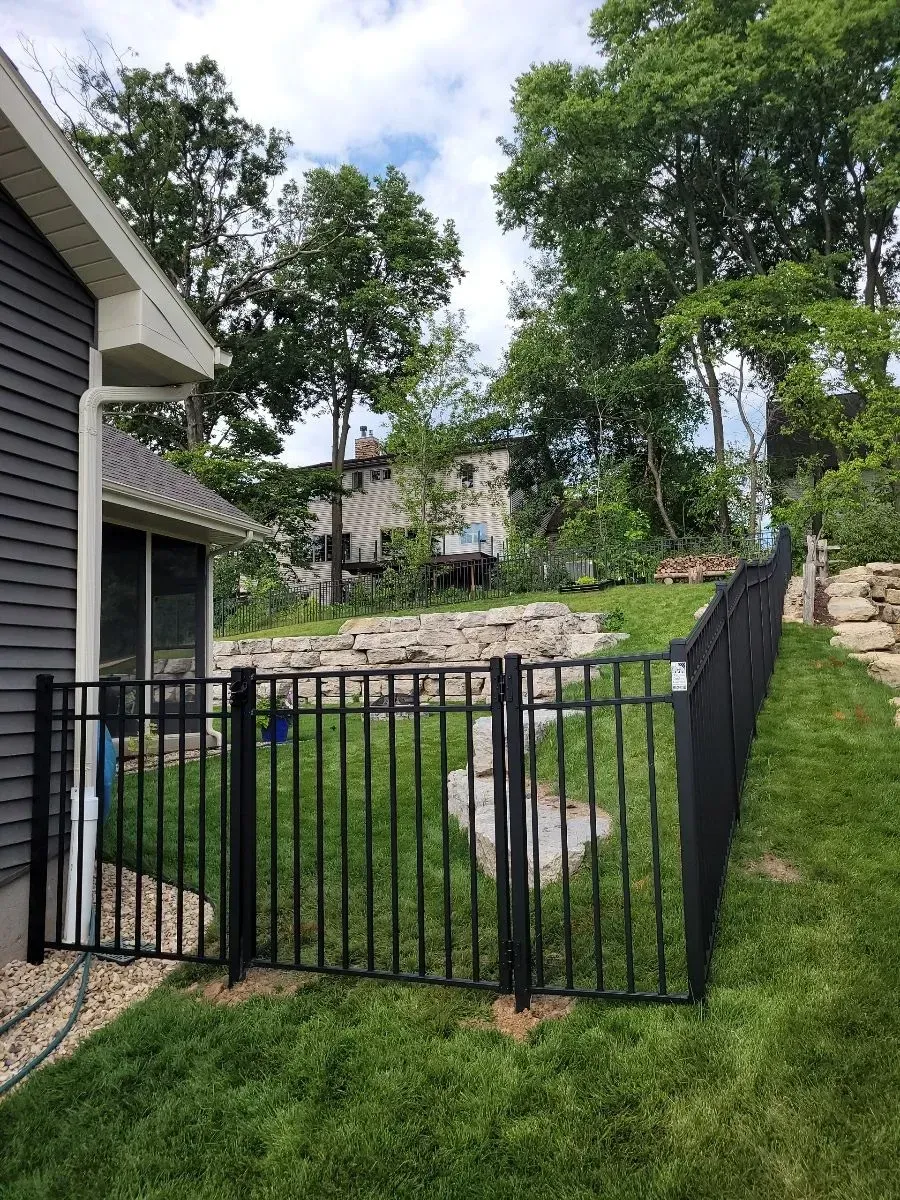 A black fence surrounds a lush green yard next to a house.