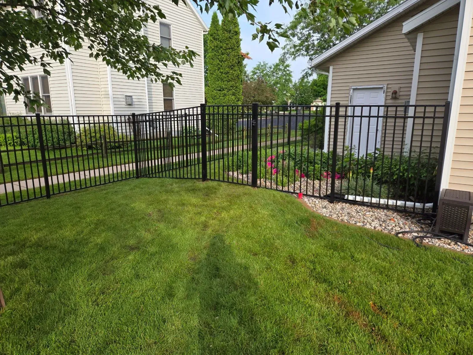 A black fence surrounds a lush green yard in front of a house.