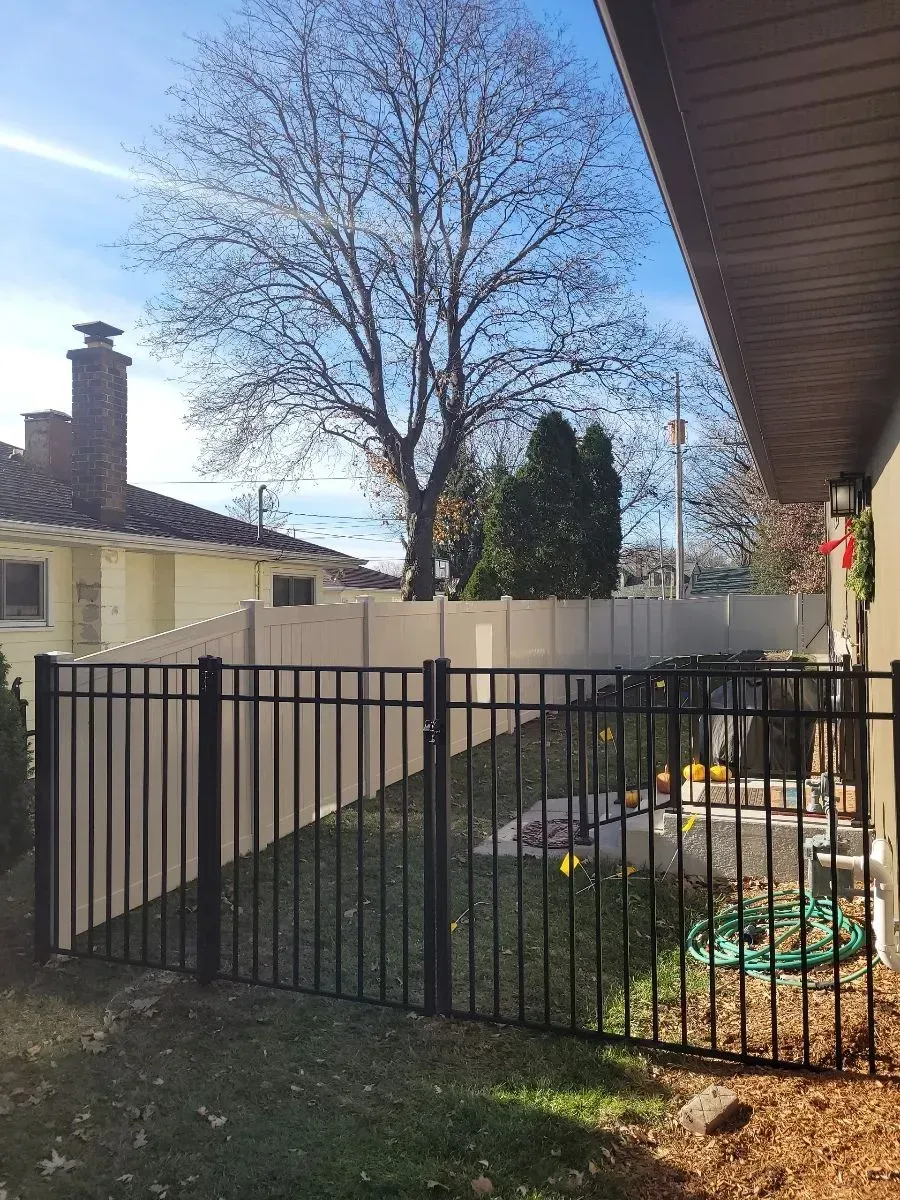 A black fence is surrounding a backyard with a white fence.