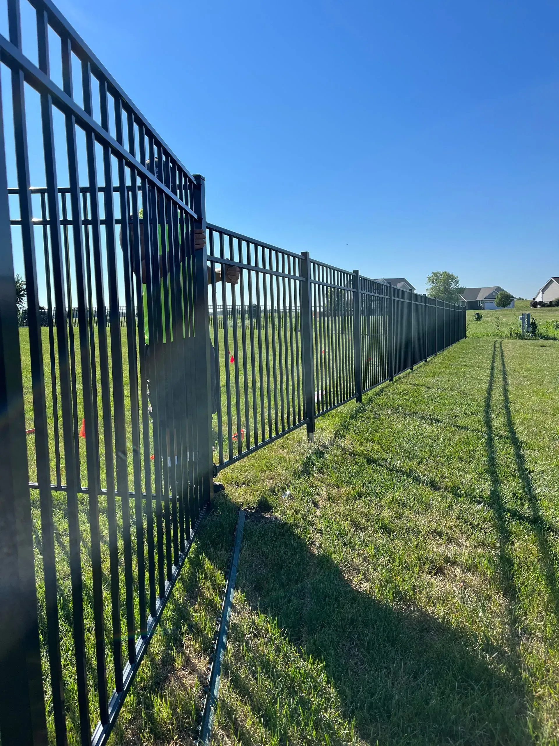 A black fence surrounds a grassy field on a sunny day.