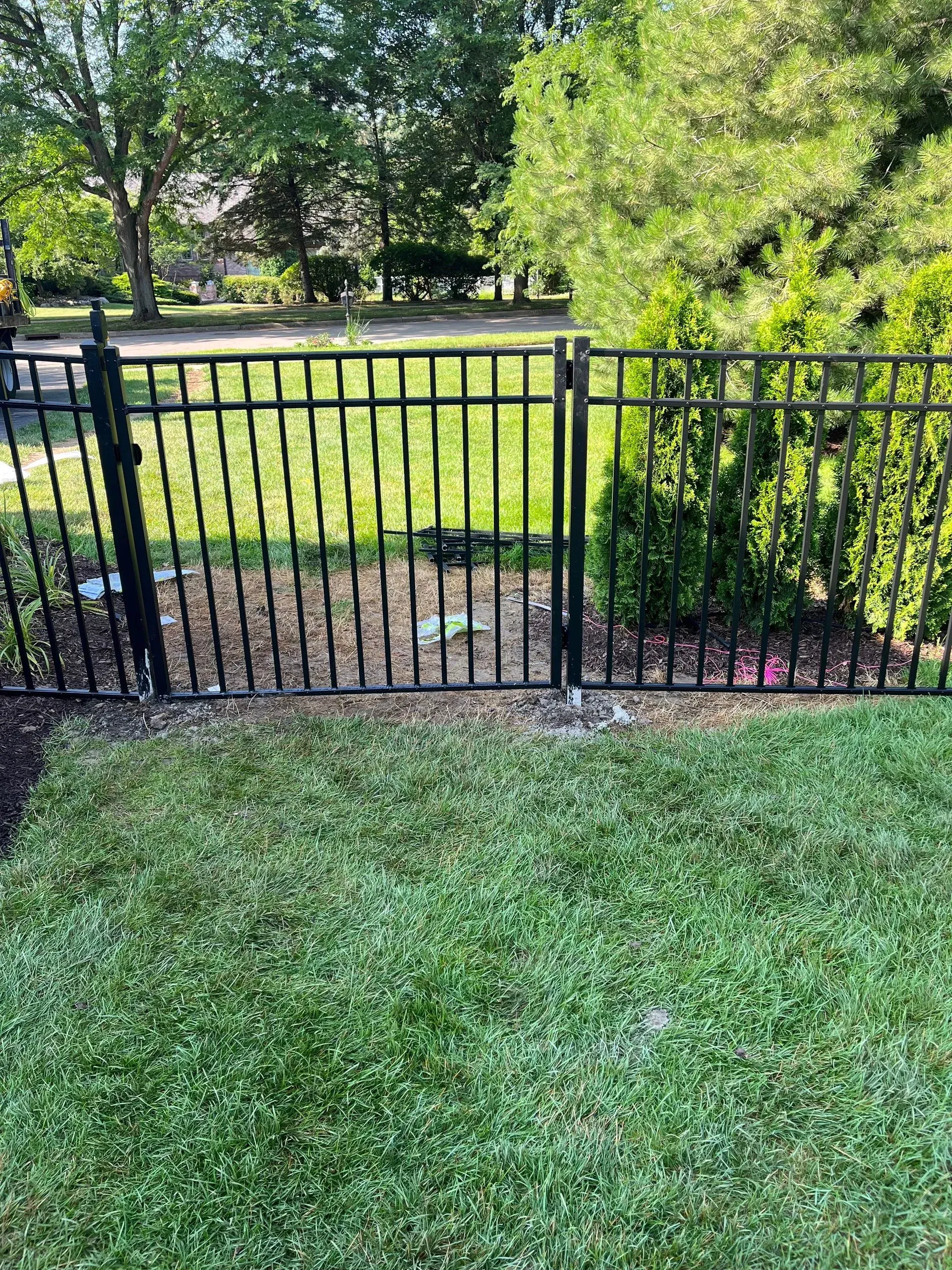 A black metal fence with a gate is in the middle of a lush green yard.