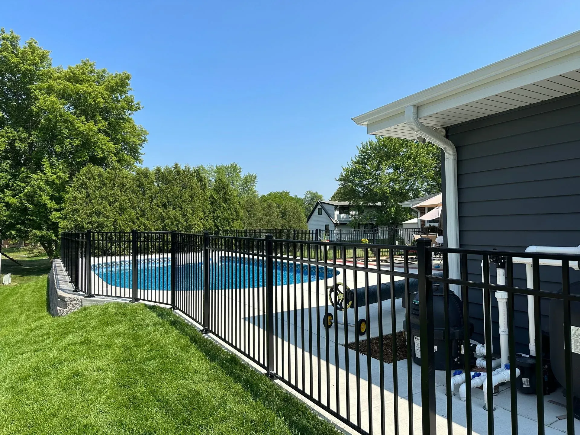 A black fence surrounds a swimming pool in a backyard.