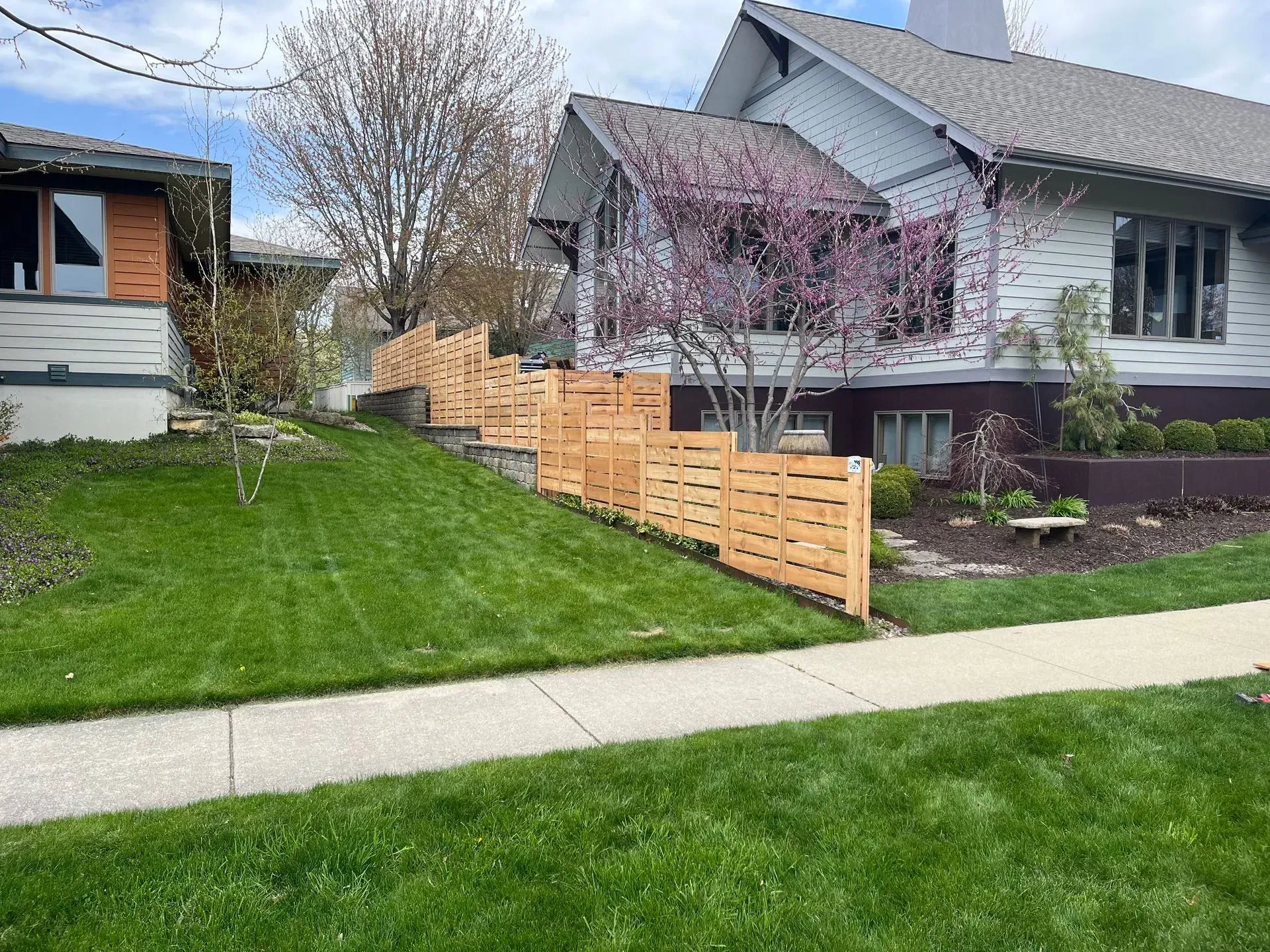 A wooden fence surrounds a lush green yard in front of a house.