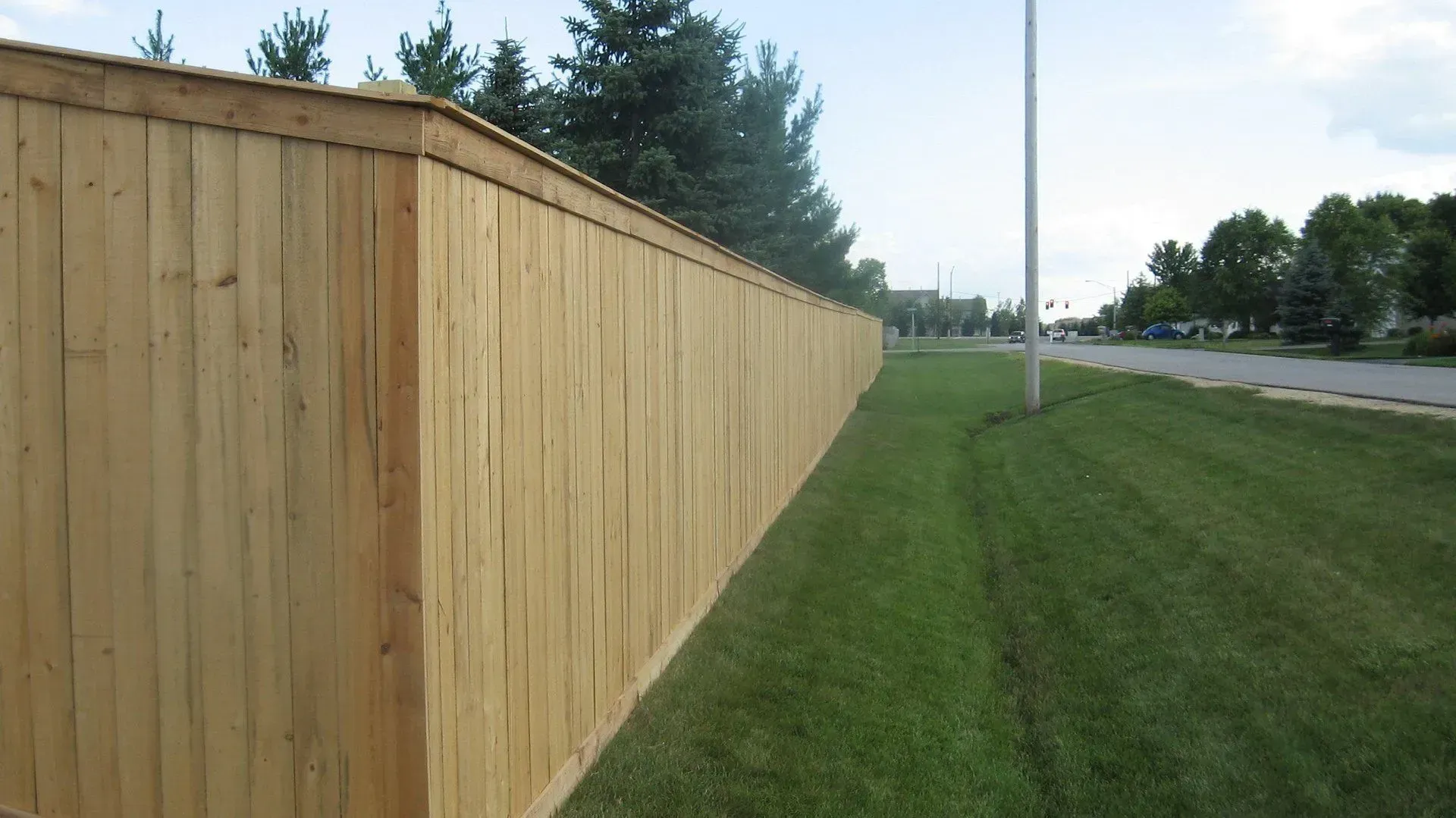 A wooden fence surrounds a lush green field next to a road.