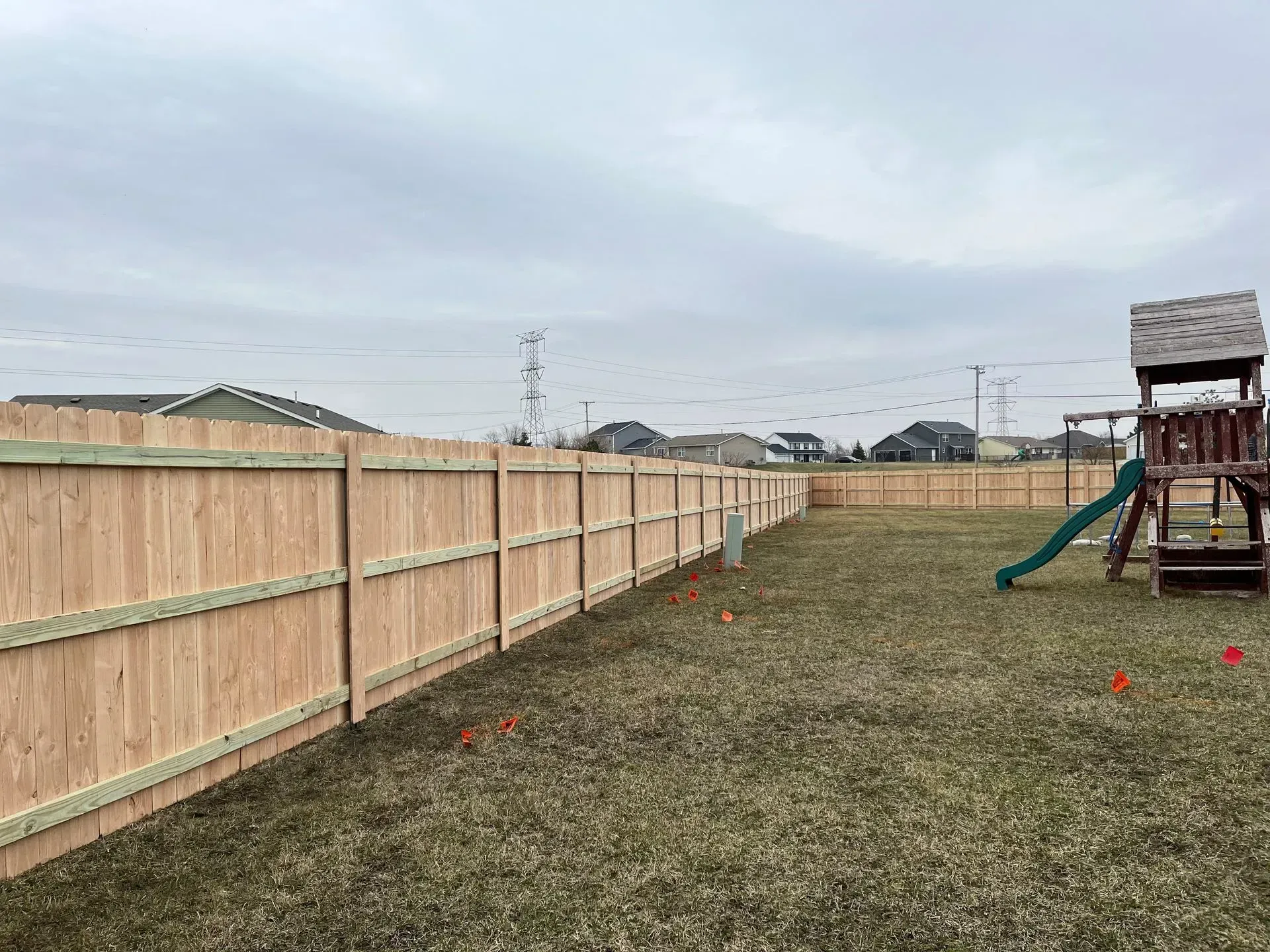 A wooden fence surrounds a playground in a backyard.