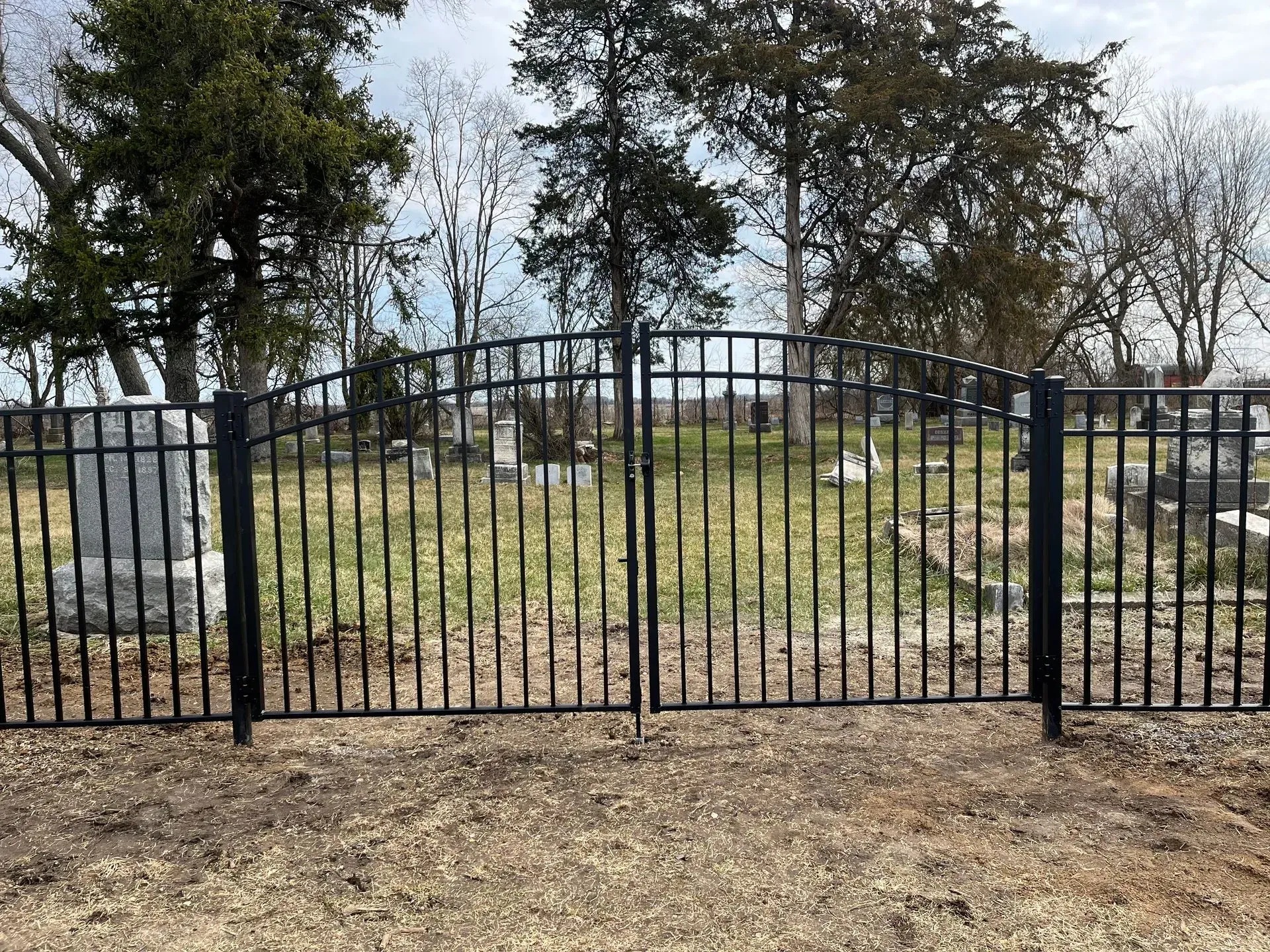 A black wrought iron fence surrounds a cemetery with trees in the background.