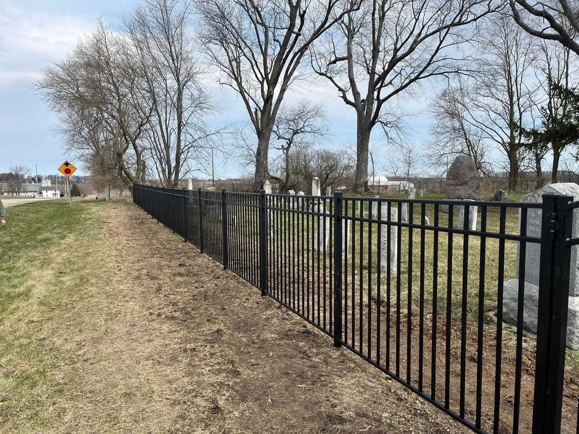 A black metal fence surrounds a cemetery with trees in the background.