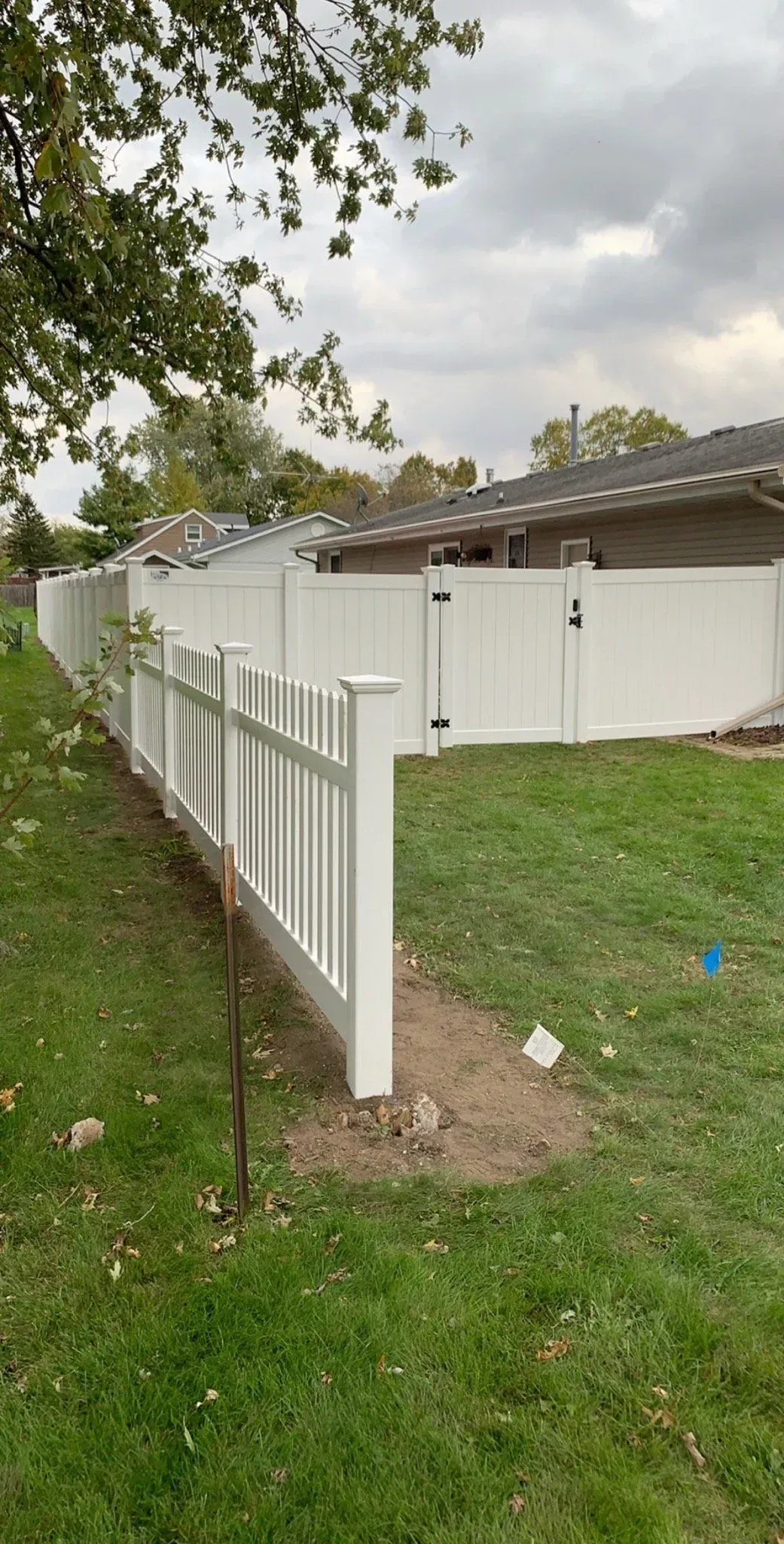 A white fence surrounds a lush green yard in front of a house.