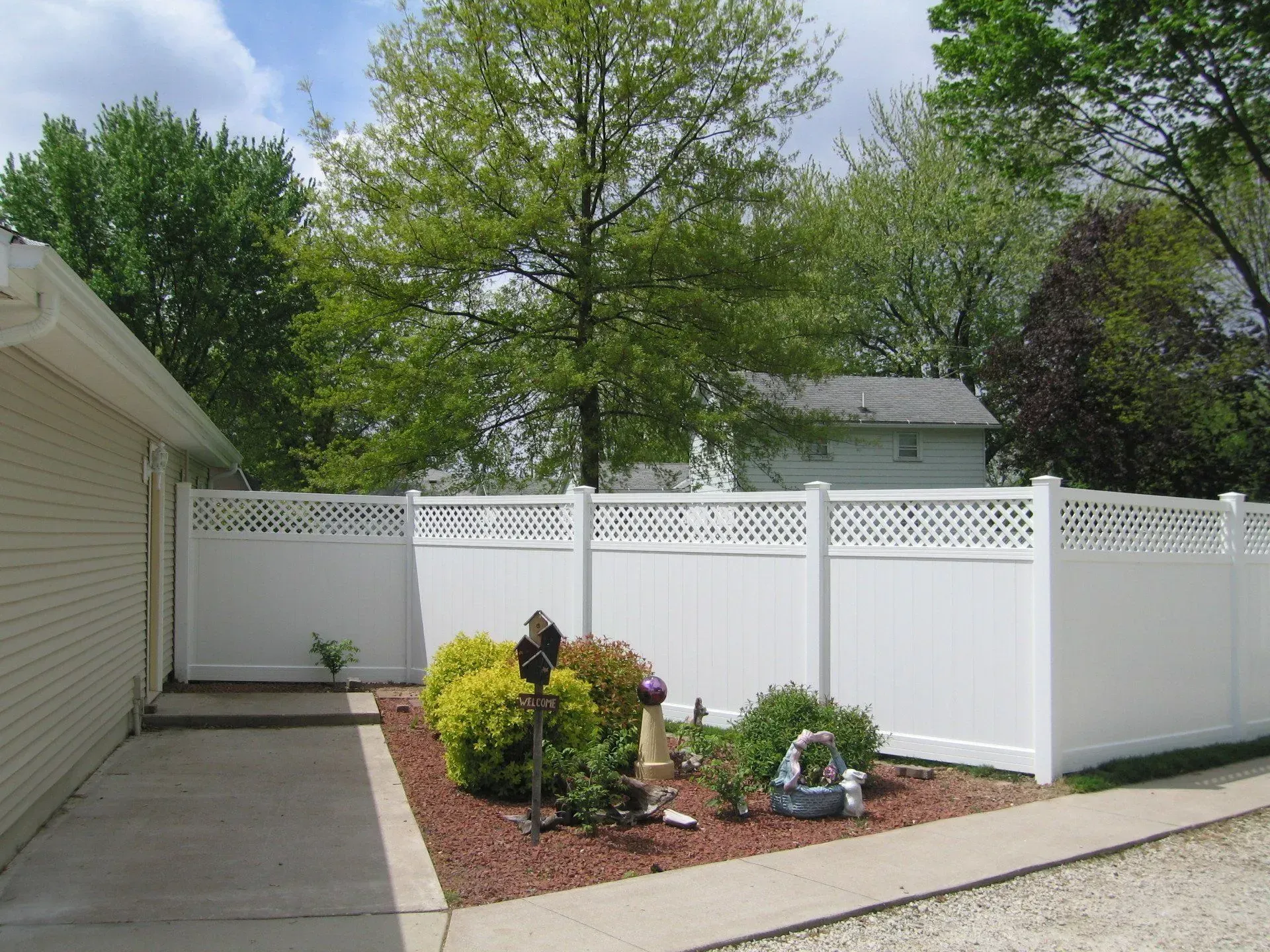 A white fence surrounds a garden in front of a house