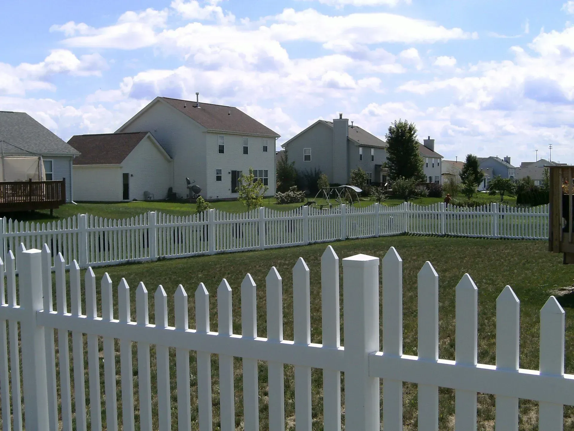 A white picket fence surrounds a residential area with houses in the background
