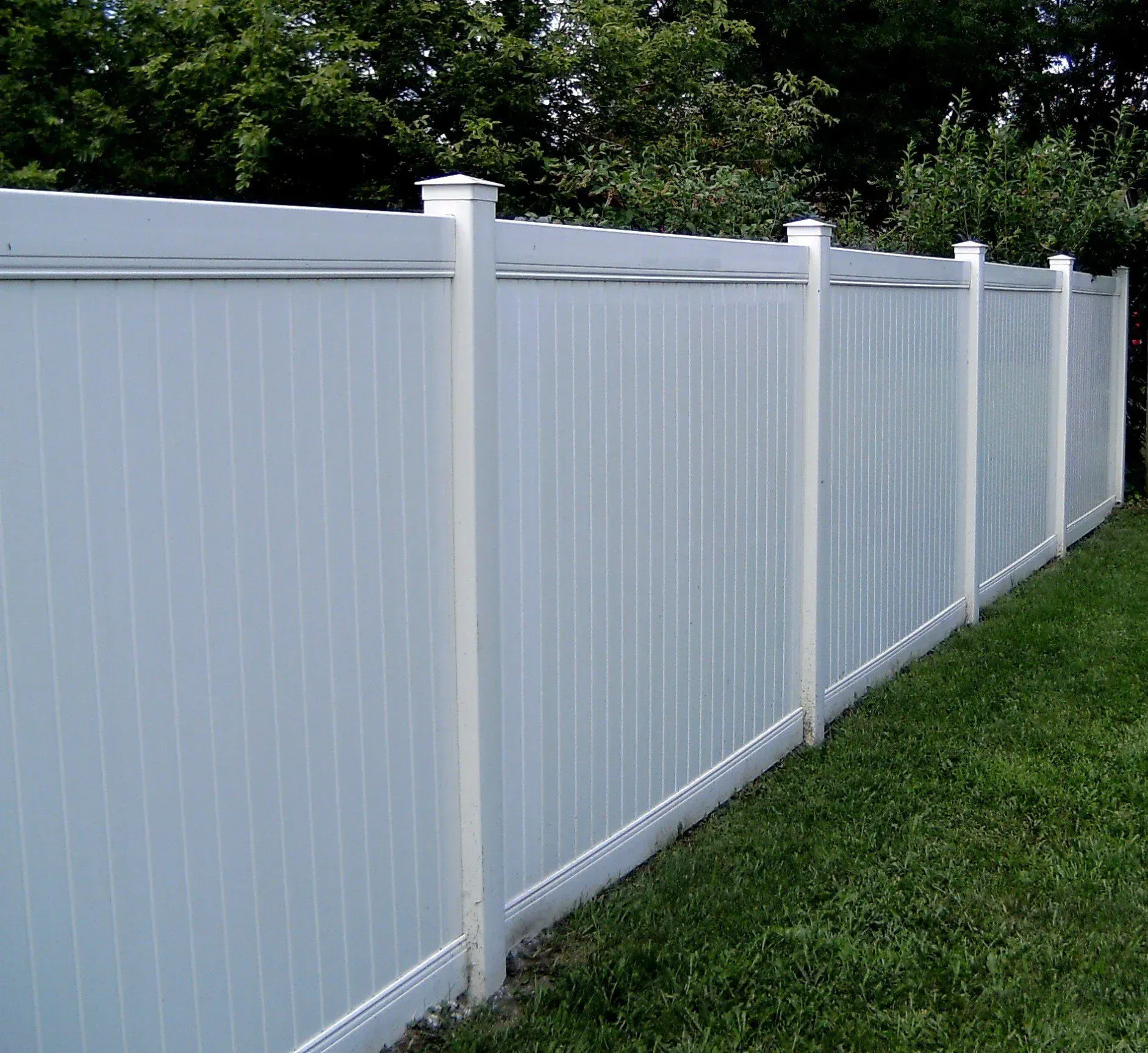A white fence is surrounded by green grass and trees