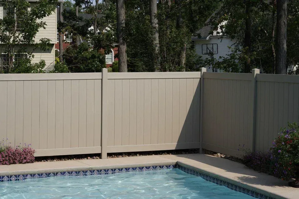A fence surrounds a swimming pool with a house in the background