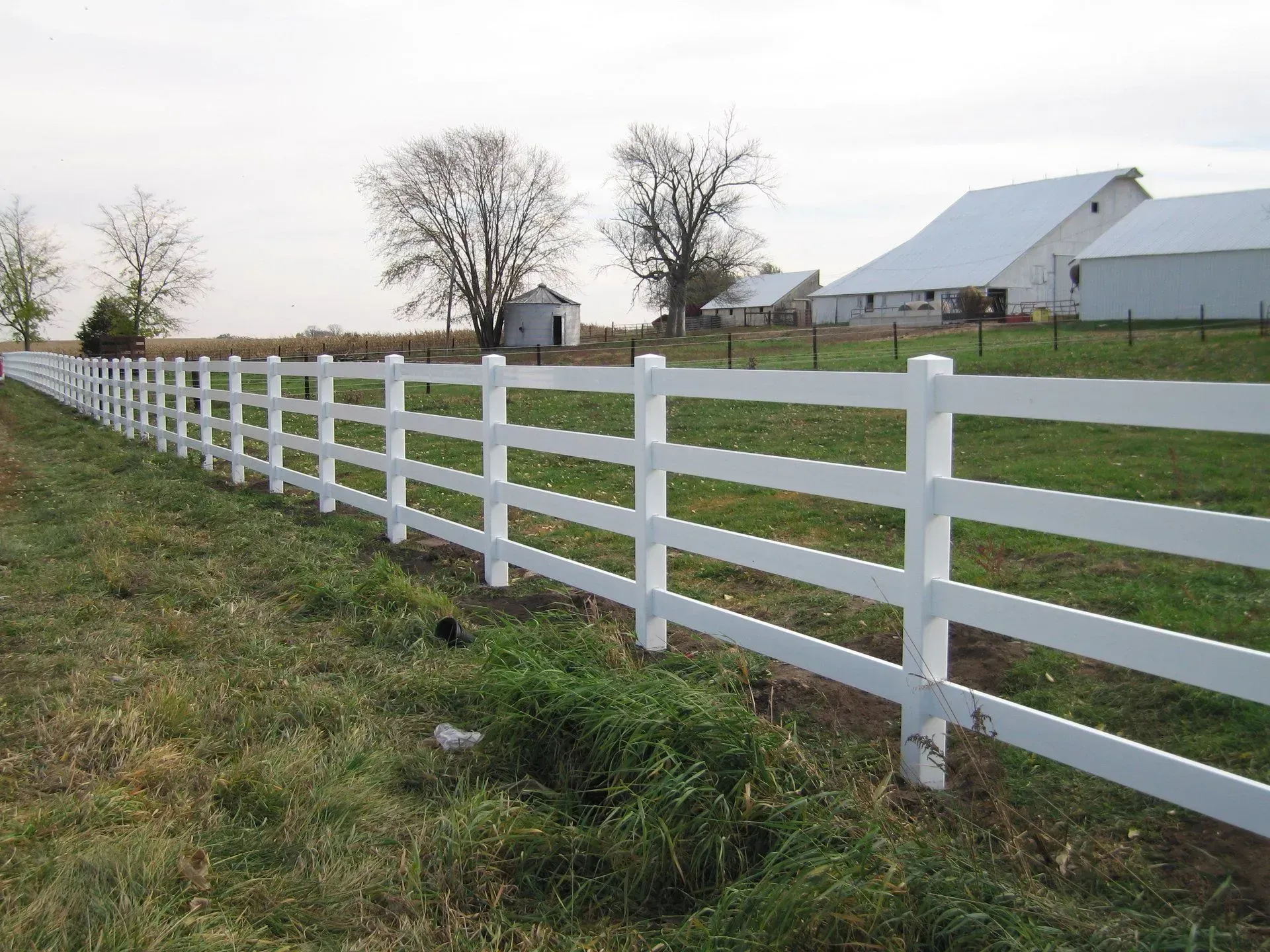 A white fence surrounds a grassy field with a barn in the background