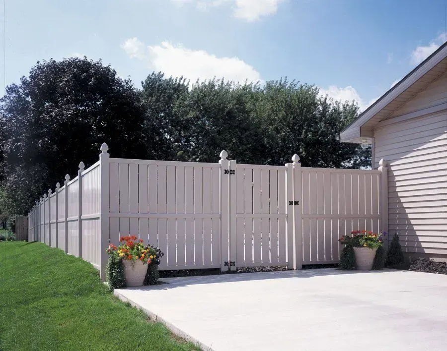 A white fence surrounds a driveway and a house