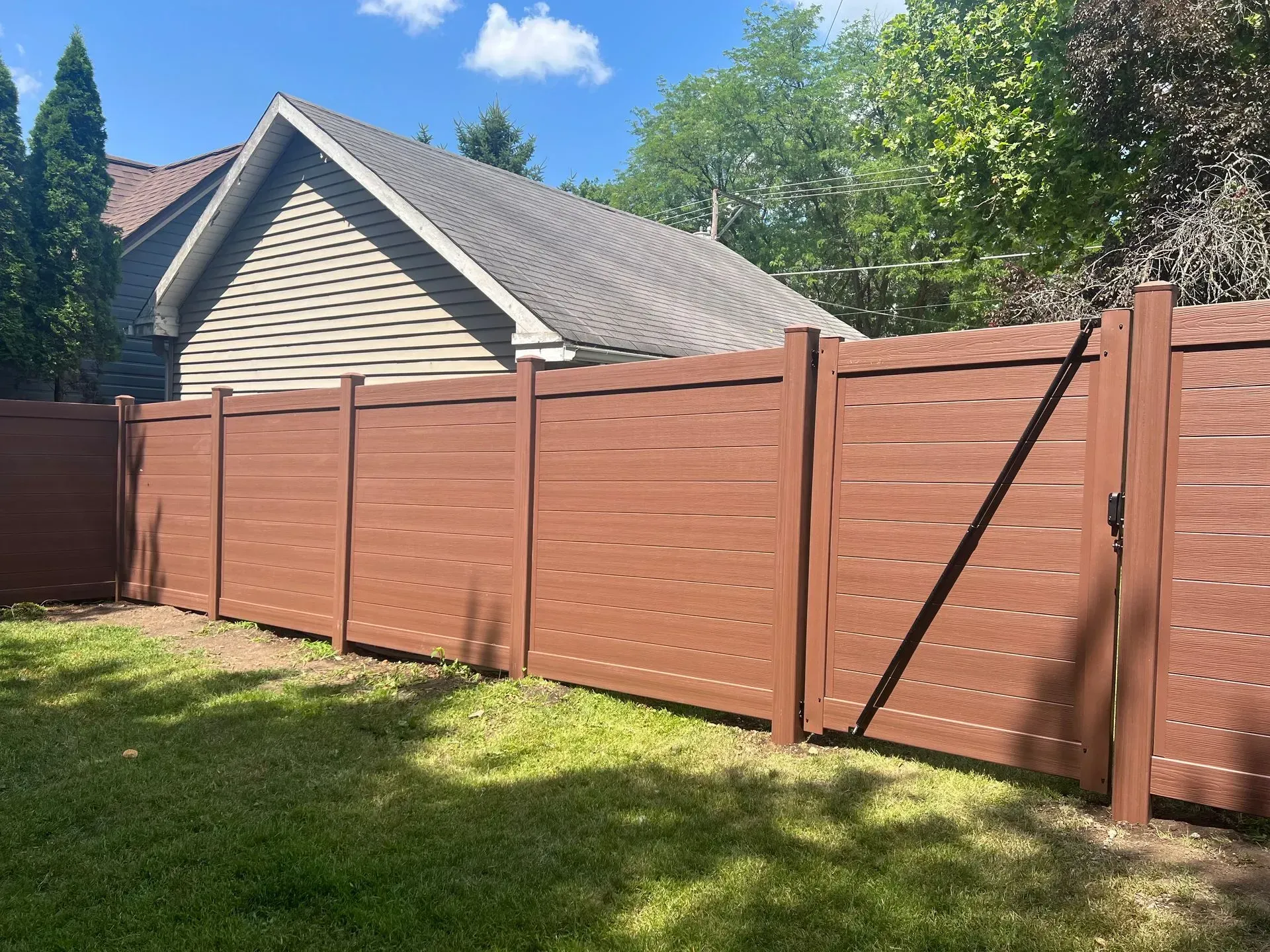 A wooden fence surrounds a lush green yard in front of a house.