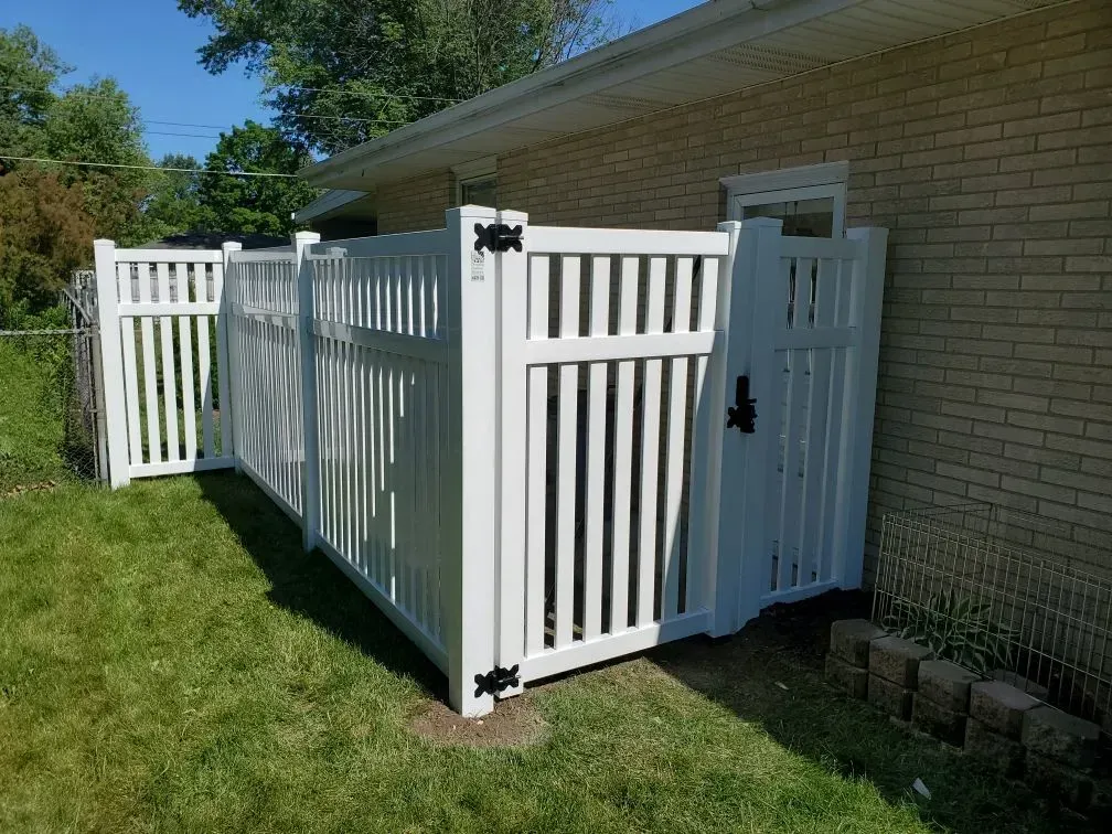 A white fence with a gate is in front of a brick house.