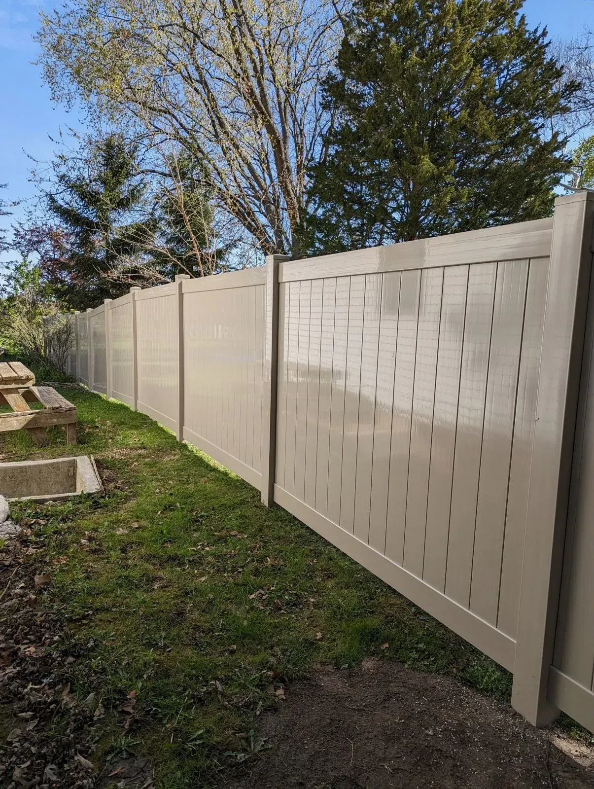 A white fence with holes in it is surrounded by grass and trees.