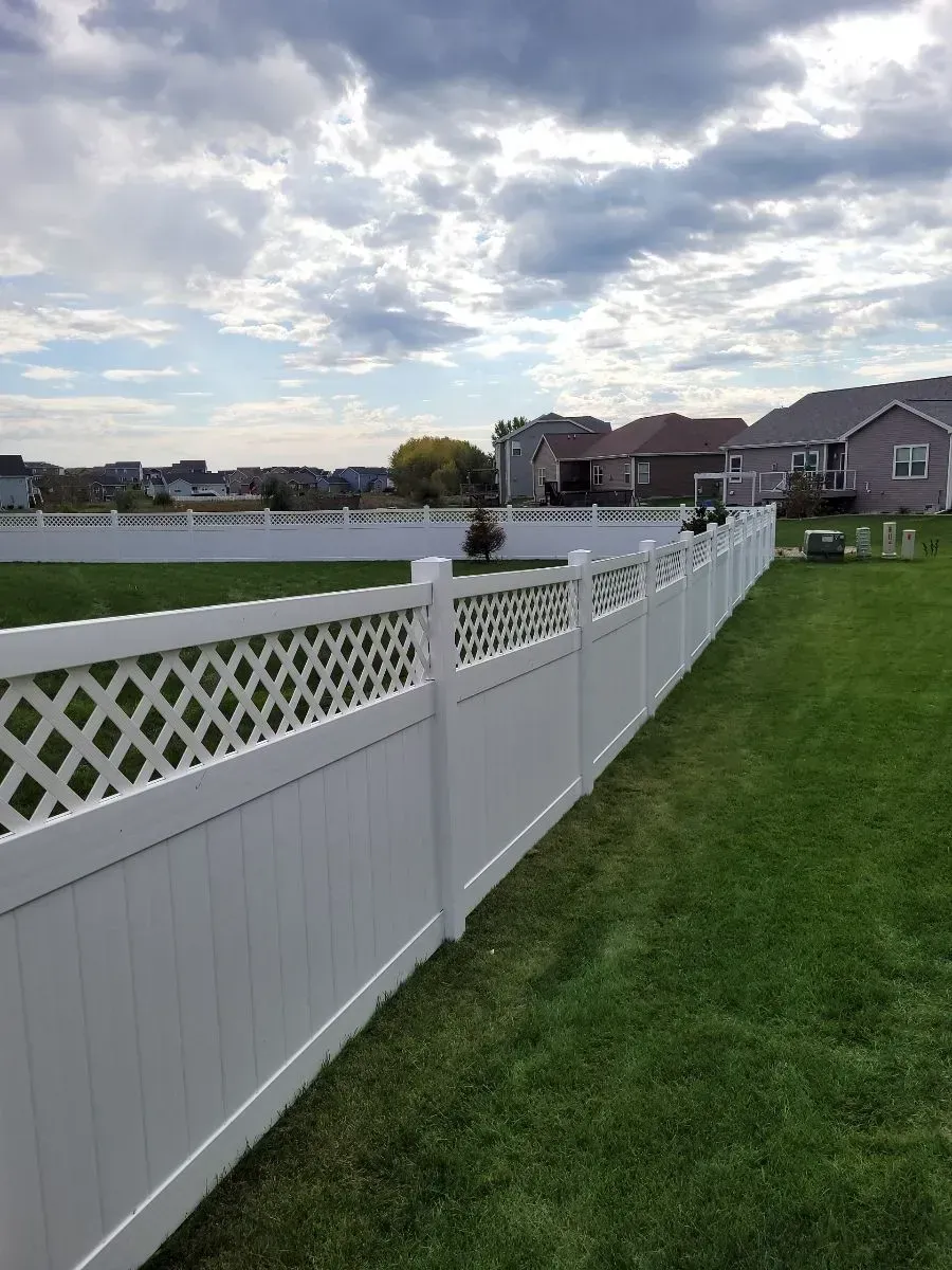A white fence surrounds a lush green lawn in a backyard.