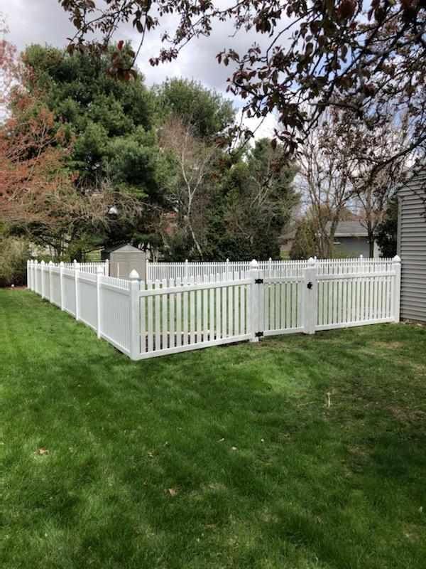 A white vinyl fence is in the middle of a lush green yard.