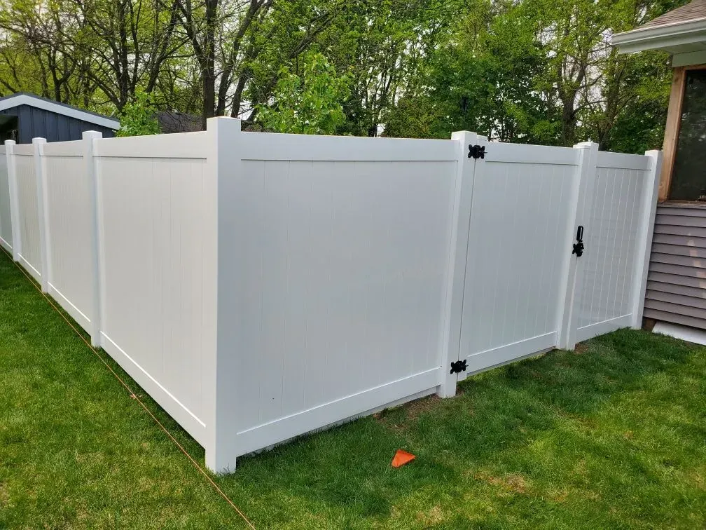 A white vinyl fence with a gate in the backyard of a house.