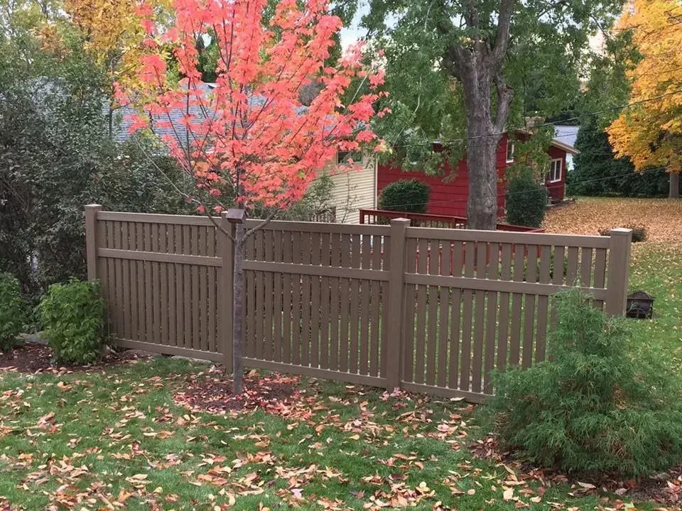 A wooden fence in a yard with a red house in the background.
