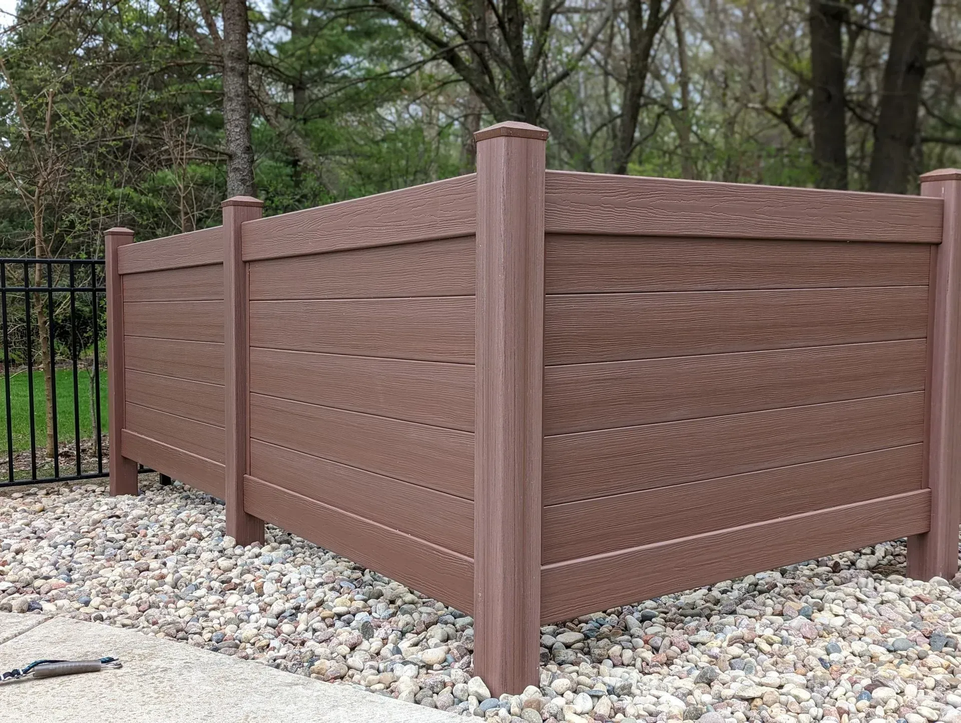 A brown wooden fence is surrounded by rocks and trees.