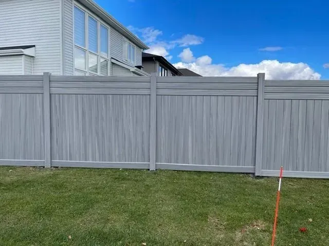 A gray fence is in the backyard of a house.