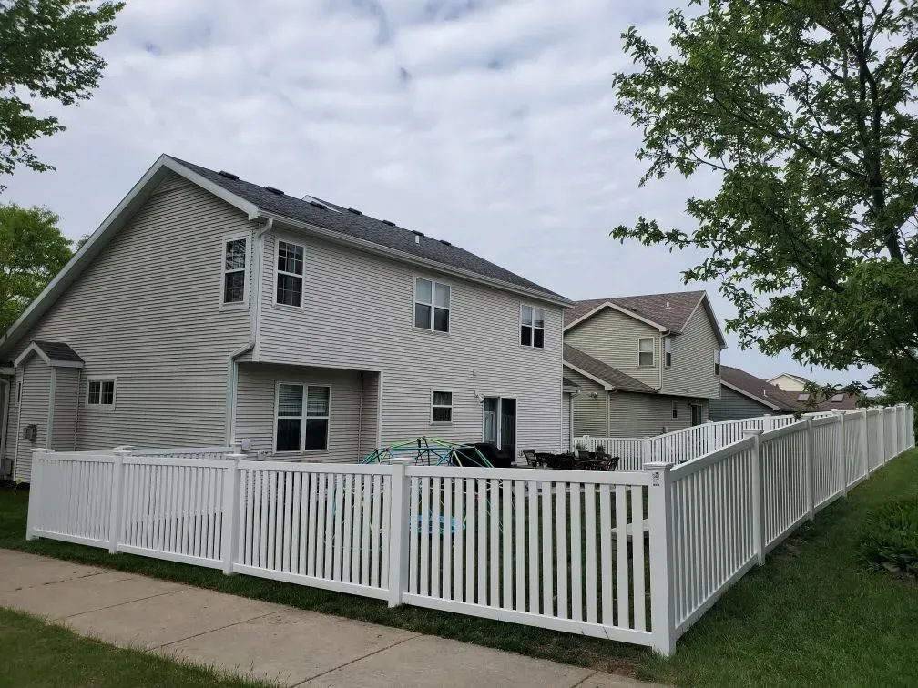 A white fence surrounds the backyard of a house.