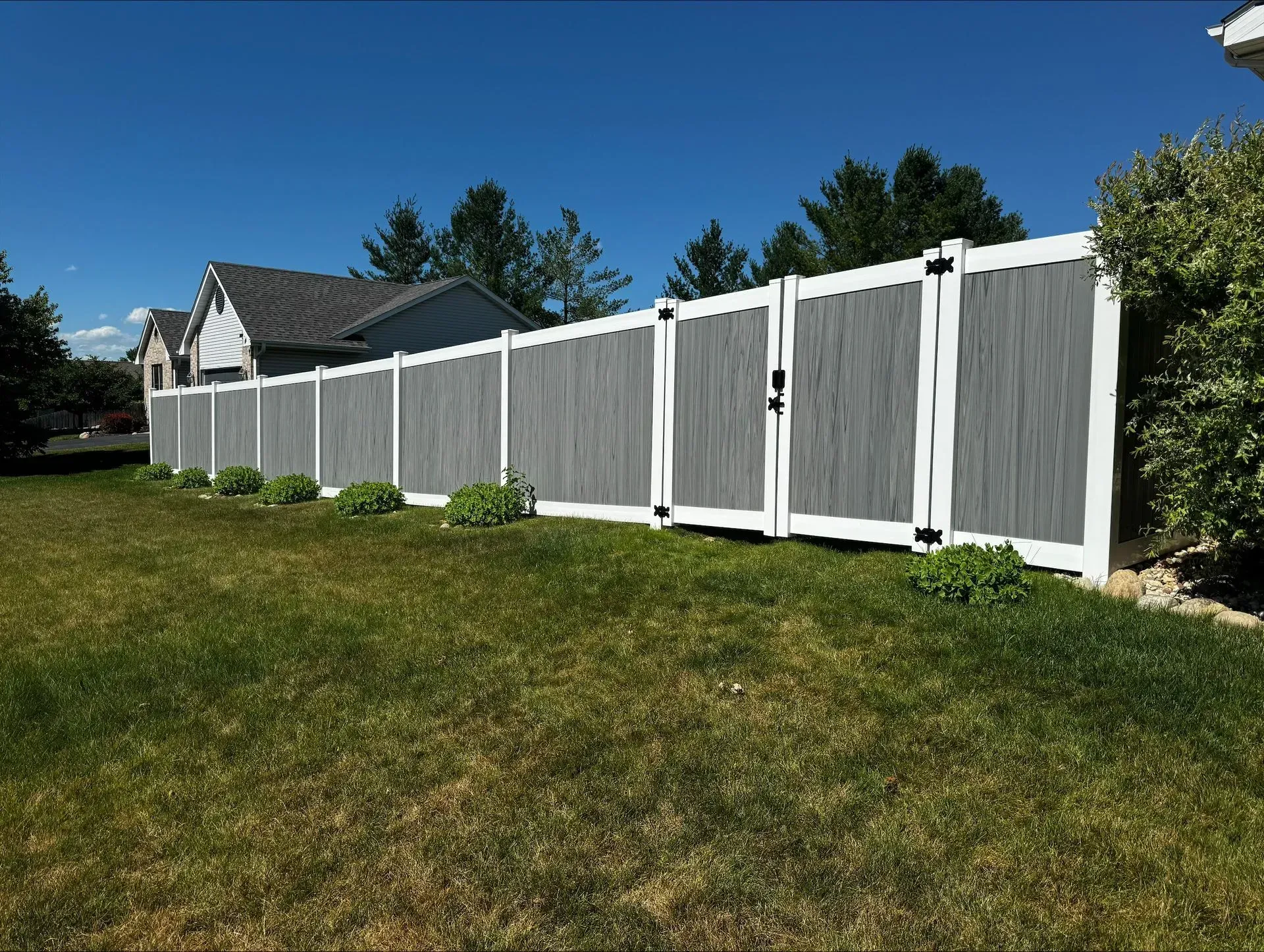 A gray and white fence with a gate in a grassy yard in front of a house.