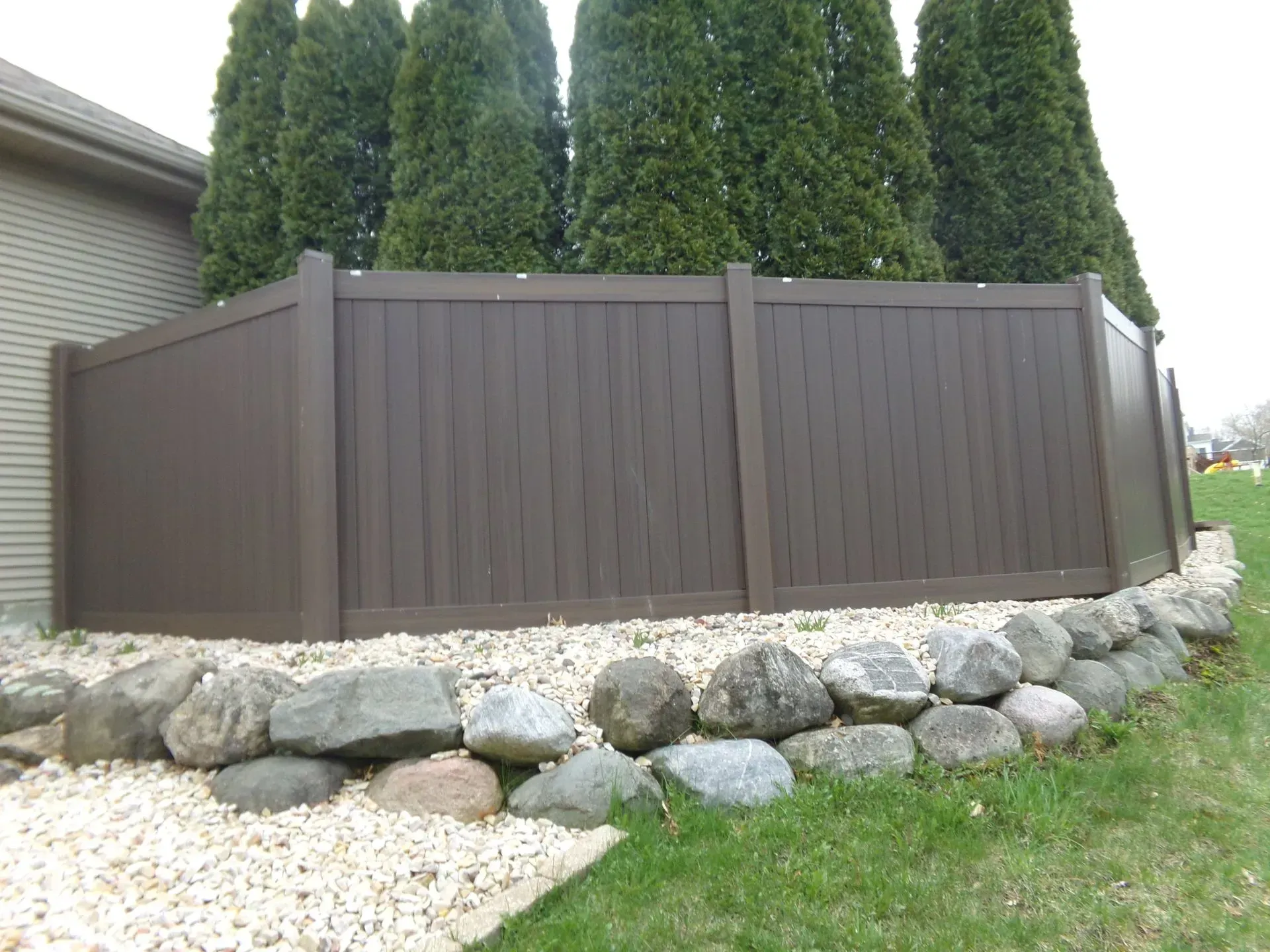 A brown fence is surrounded by rocks and trees.