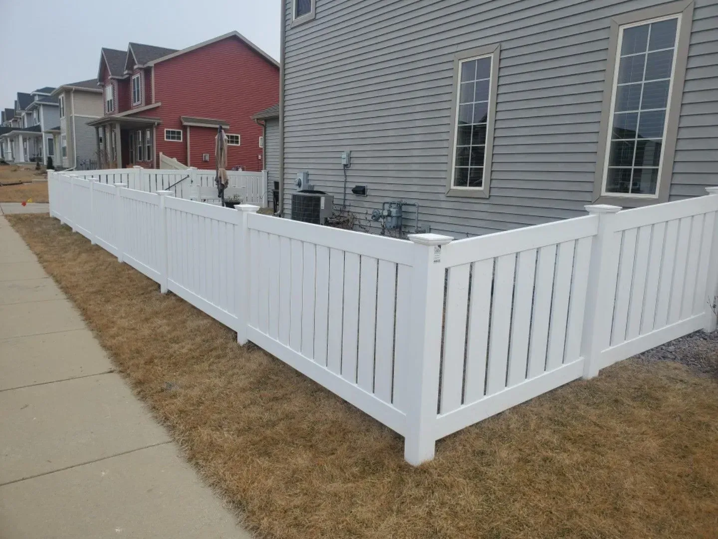 A white fence is surrounding a house in a residential area.