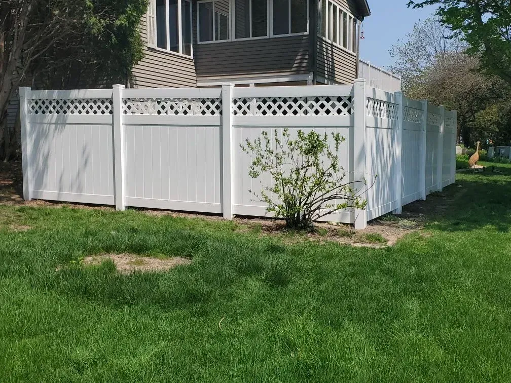 A white fence surrounds a lush green yard in front of a house.