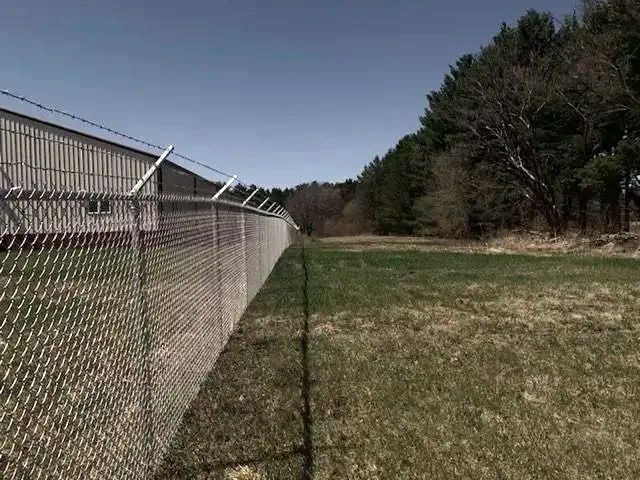 A chain link fence surrounds a field with trees in the background.