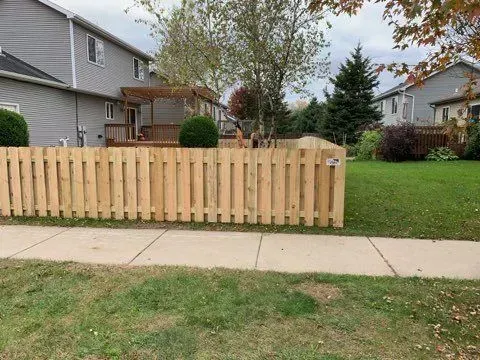 A wooden fence surrounds a lush green yard in front of a house.