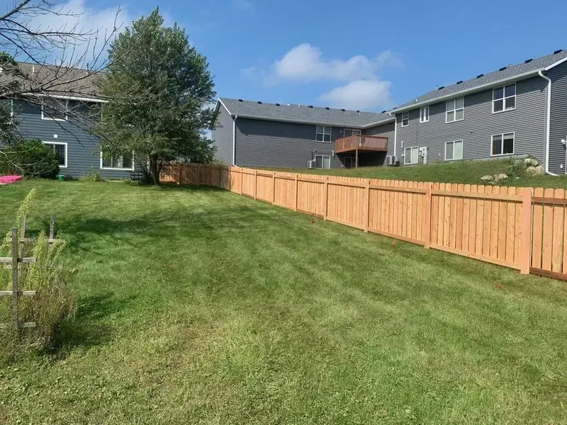 A wooden fence surrounds a lush green lawn in front of a house.